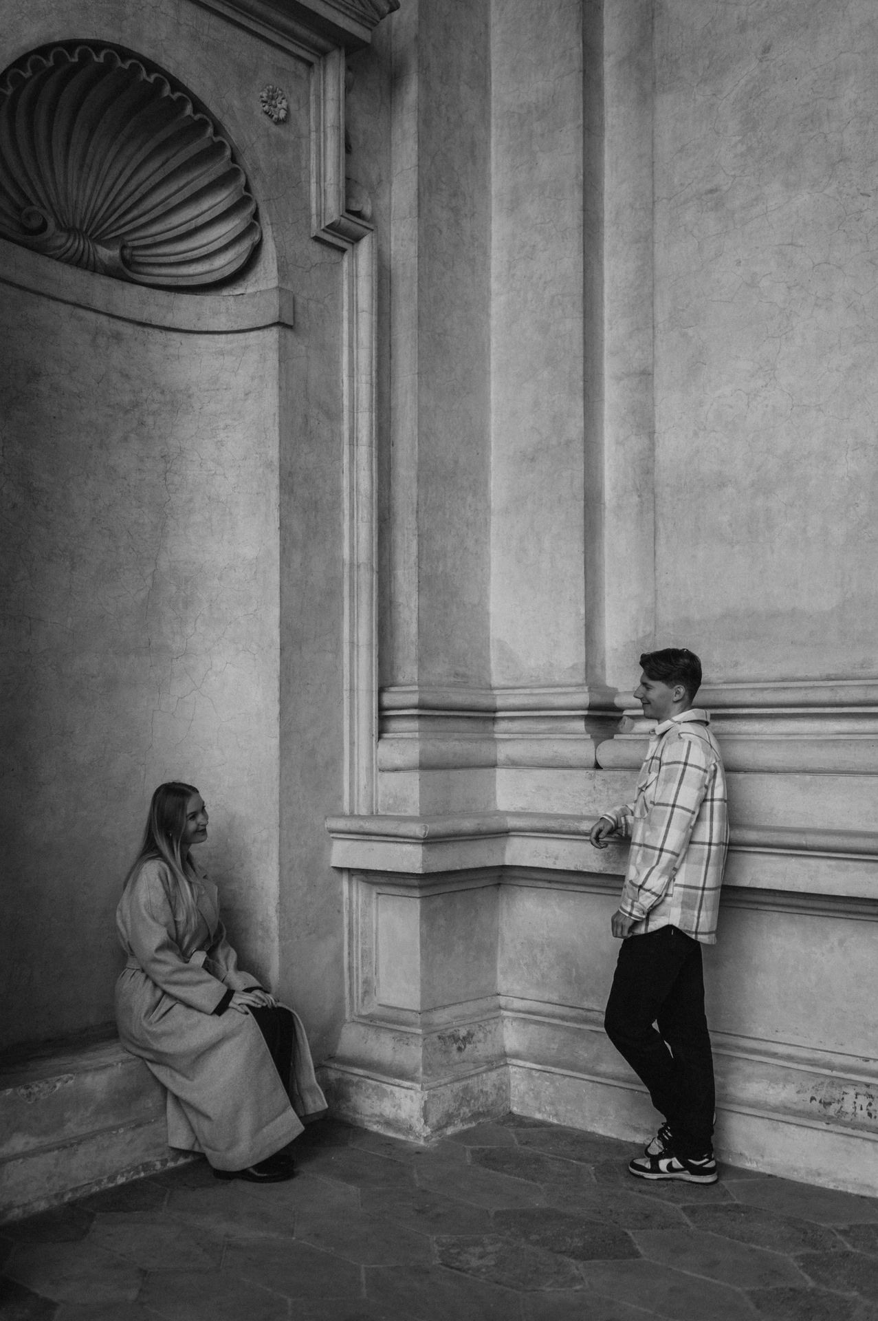 Black-and-white portrait of the couple facing each other from an alcove and a stone column during their Prague couple photoshoot.