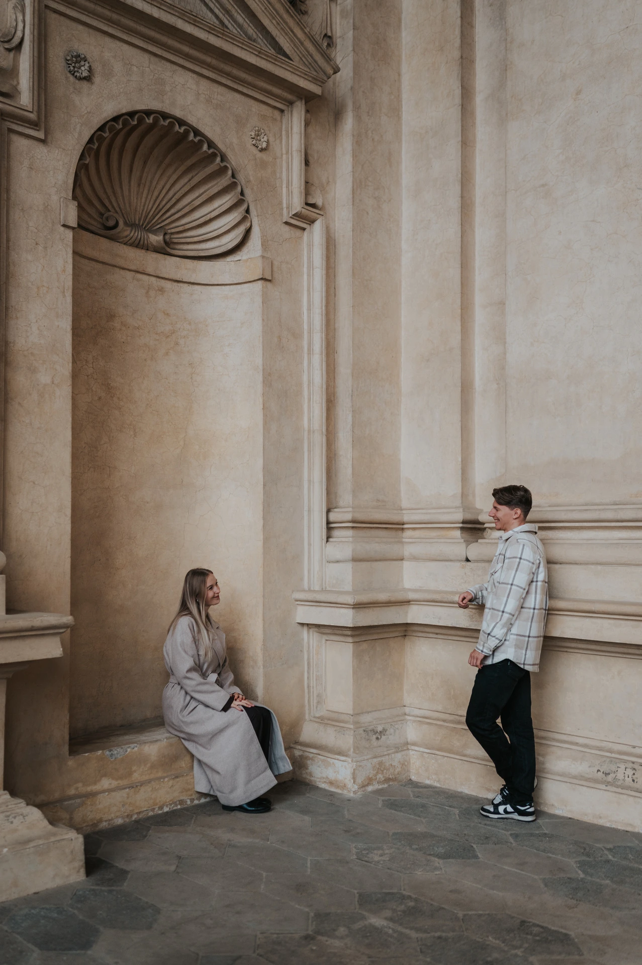 Couple facing each other beside a shell-topped alcove and stone column during their Prague couple photoshoot.