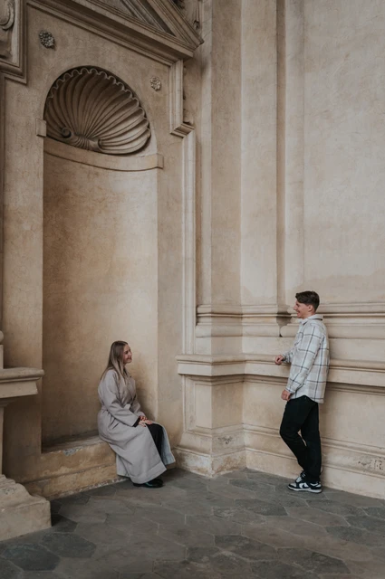 Prague couple photoshoot: an alcove and a column in Wallenstein Garden Couple facing each other beside a shell-topped alcove and stone column during their Prague couple photoshoot.