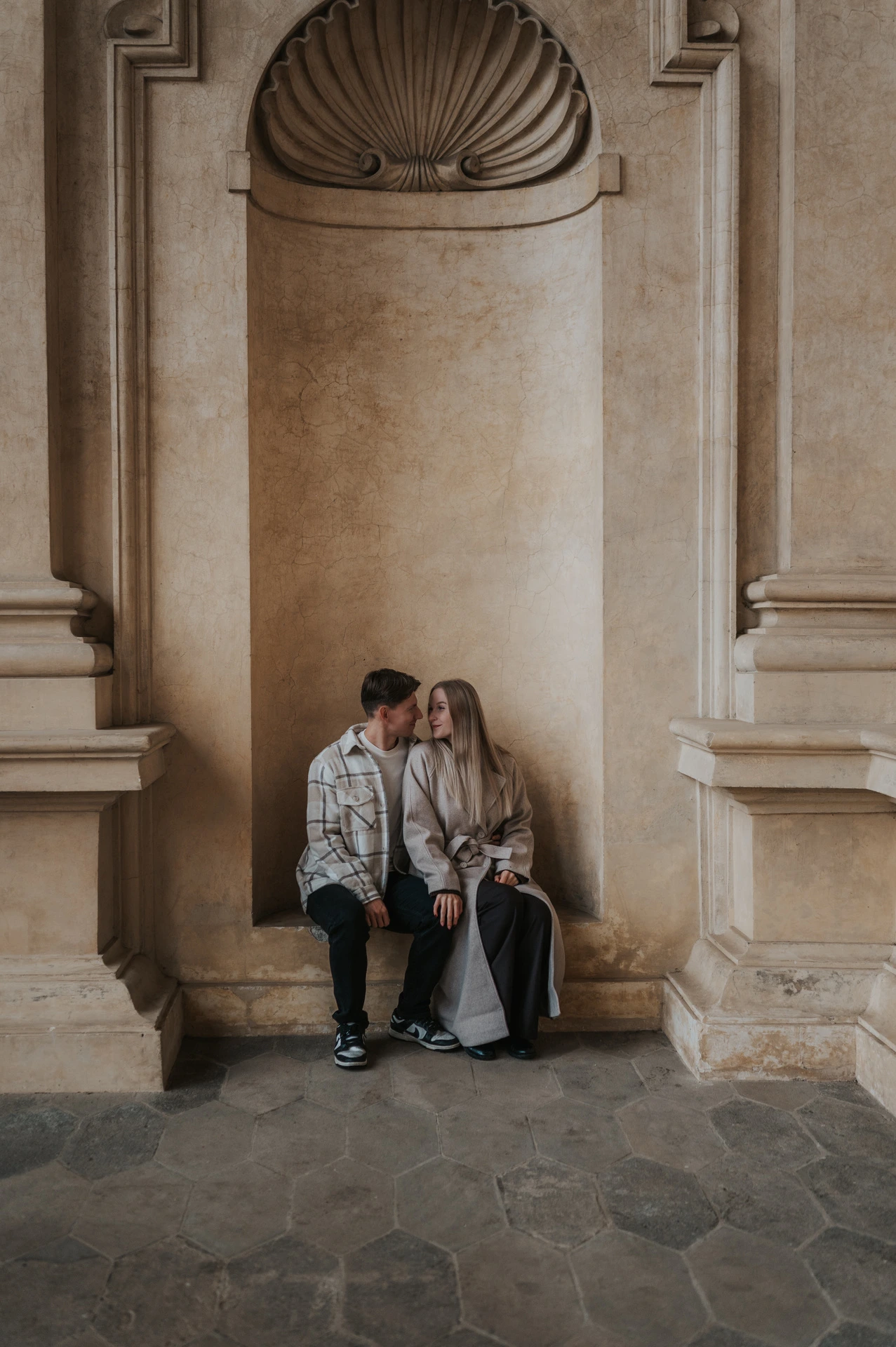 Couple kissing while seated in a tall shell-topped alcove at Wallenstein Garden during their Prague couple photoshoot.
