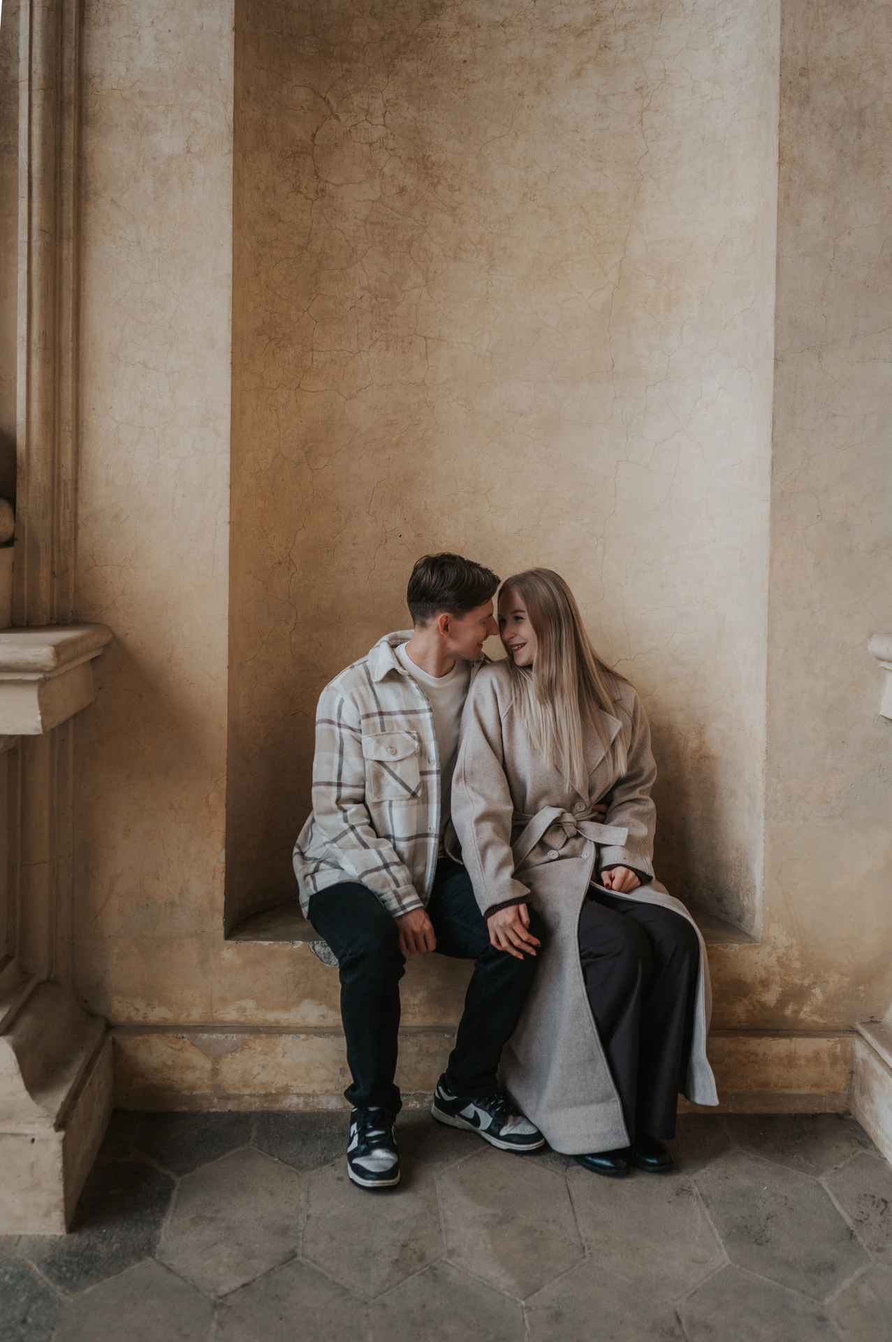 Couple leaning together on a stone bench in an alcove at Wallenstein Garden during their Prague couple photoshoot.