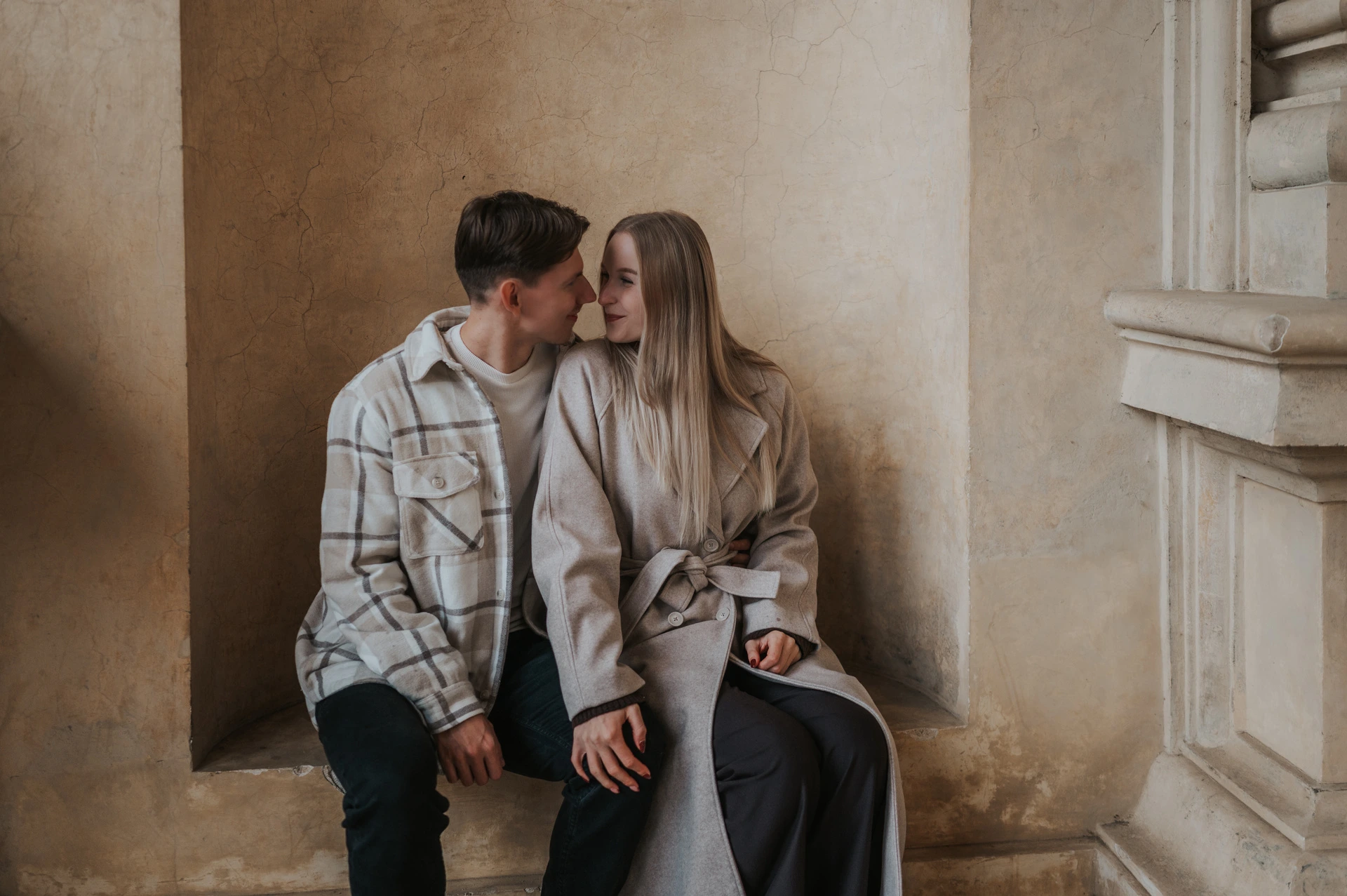 Wide photograph of the couple sharing a kiss on a stone alcove bench during their Prague couple photoshoot.