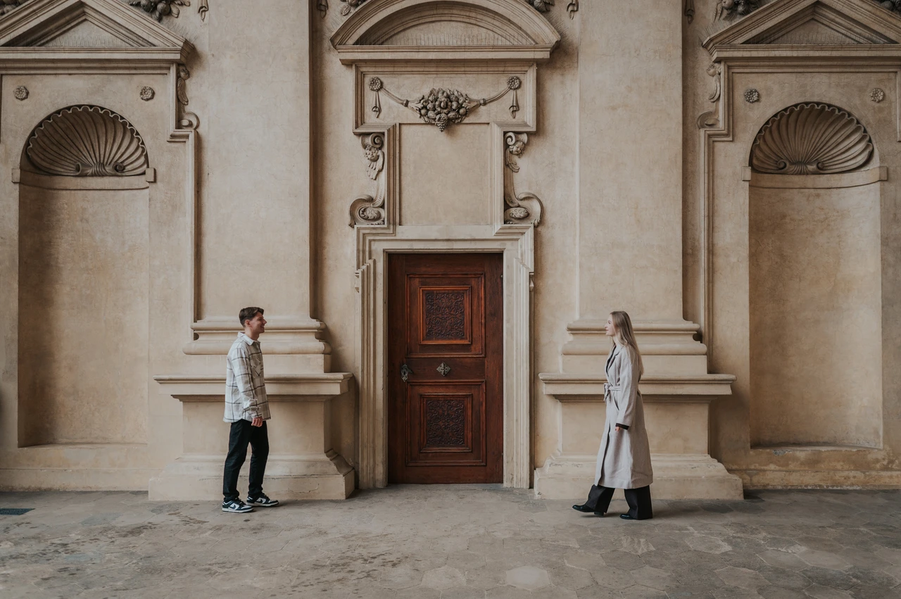 Prague couple photoshoot: facing each other across the arcade doorway Wide view of the couple facing each other across an ornate wooden doorway during their Prague couple photoshoot.