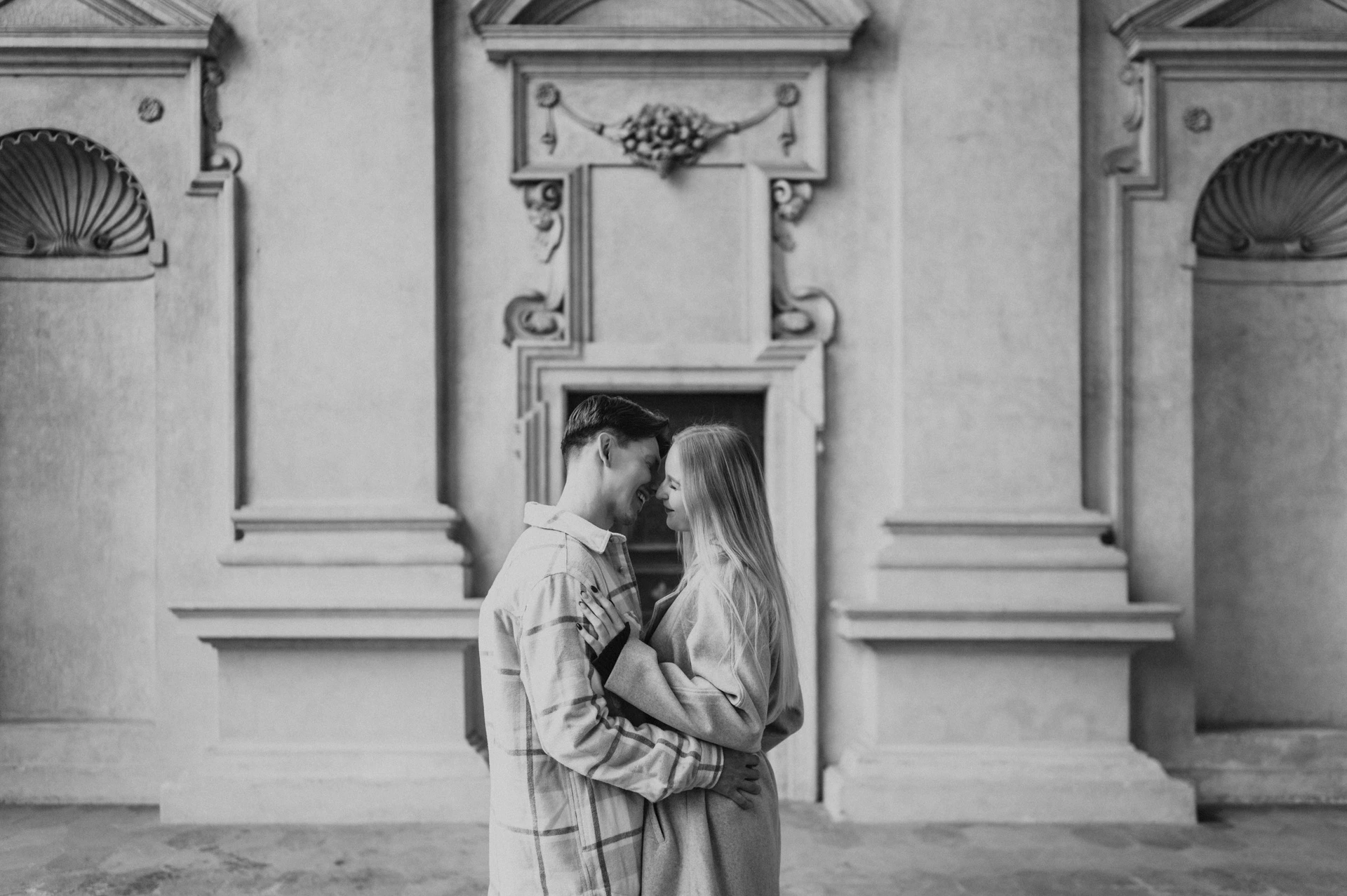Black-and-white photograph of the couple embracing beside decorated arcade walls during their Prague couple photoshoot.