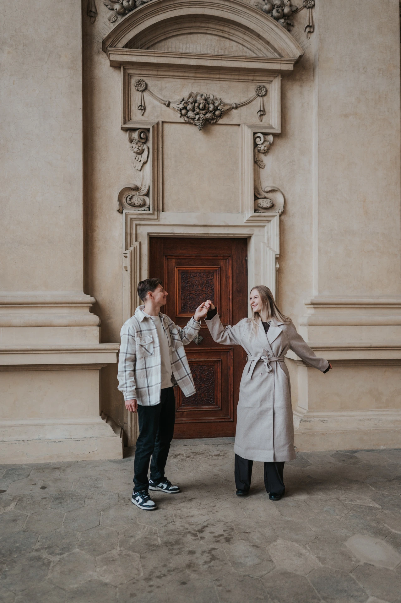 Couple holding hands with their arms out beside the ornate garden arcade doorway during their Prague couple photoshoot.