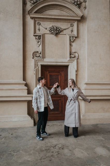 Couple holding hands with their arms out beside the ornate garden arcade doorway during their Prague couple photoshoot.