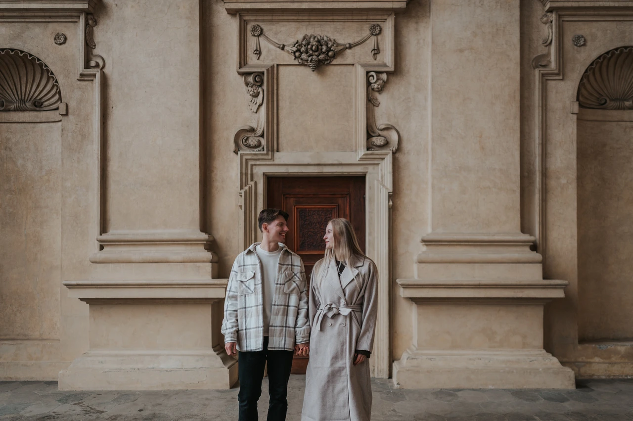 Prague couple photoshoot: together beneath the arcade decorations Couple standing together beneath the ornate wall decorations of the Wallenstein Garden arcade during their Prague couple photoshoot.