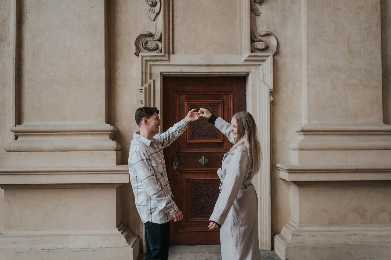 Prague couple photoshoot: a twirl beneath the arcade decorations Man lifting his partner's hand as she turns in front of the arcade doorway during their Prague couple photoshoot.
