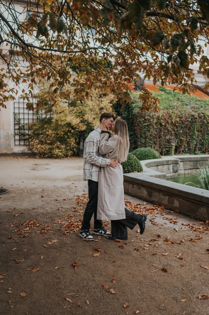 Couple kissing beside a garden balustrade beneath an autumn tree during their Prague couple photoshoot.