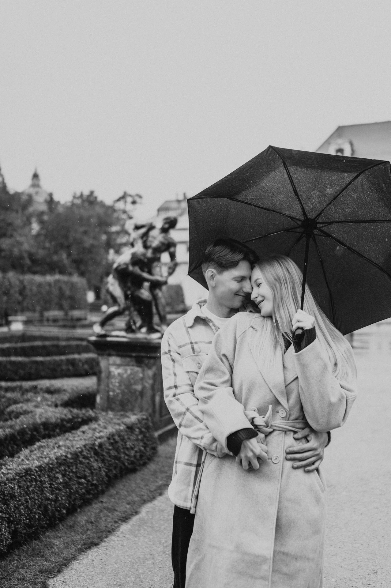 Black-and-white portrait of a cheek kiss and a smile beneath the couple's umbrella during their Prague couple photoshoot.