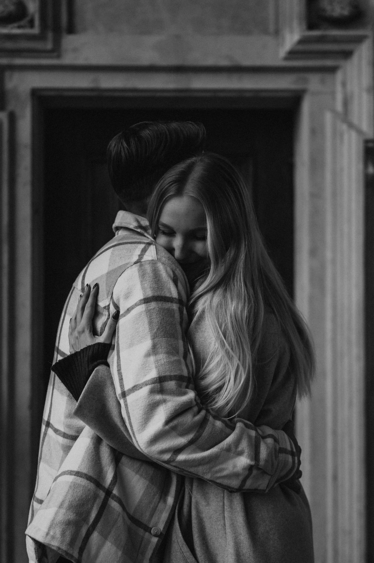 Black-and-white portrait of the woman smiling over her partner's shoulder in an embrace during their Prague couple photoshoot.