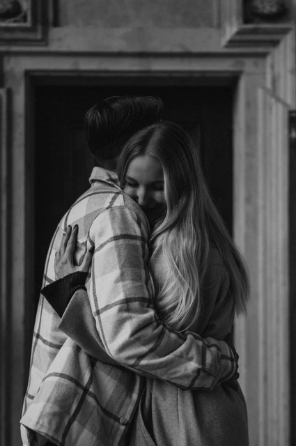 Prague couple photoshoot: a black-and-white hug in the arcade Black-and-white portrait of the woman smiling over her partner's shoulder in an embrace during their Prague couple photoshoot.