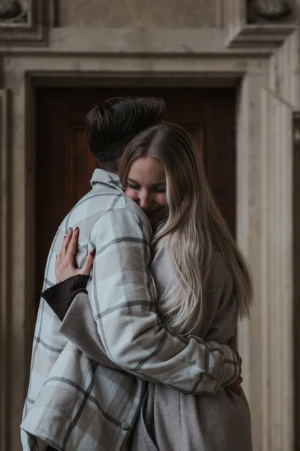 Prague couple photoshoot: a close hug in the sheltered arcade Close portrait of the woman smiling over her partner's shoulder as they hug during their Prague couple photoshoot.