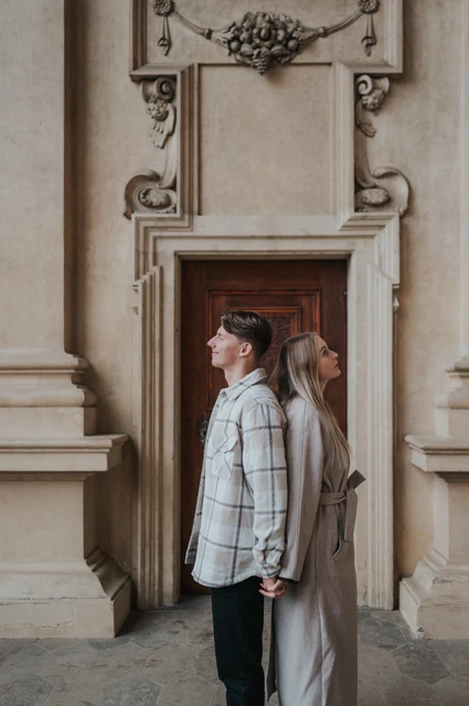 Prague couple photoshoot: a side portrait by the carved wooden door Man looking to the side with his partner standing behind him beside a carved doorway during their Prague couple photoshoot.