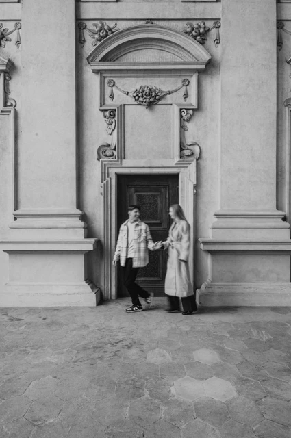 Prague couple photoshoot: holding hands outside the arcade doorway Black-and-white full-length photograph of the couple holding hands outside the arcade doorway during their Prague couple photoshoot.