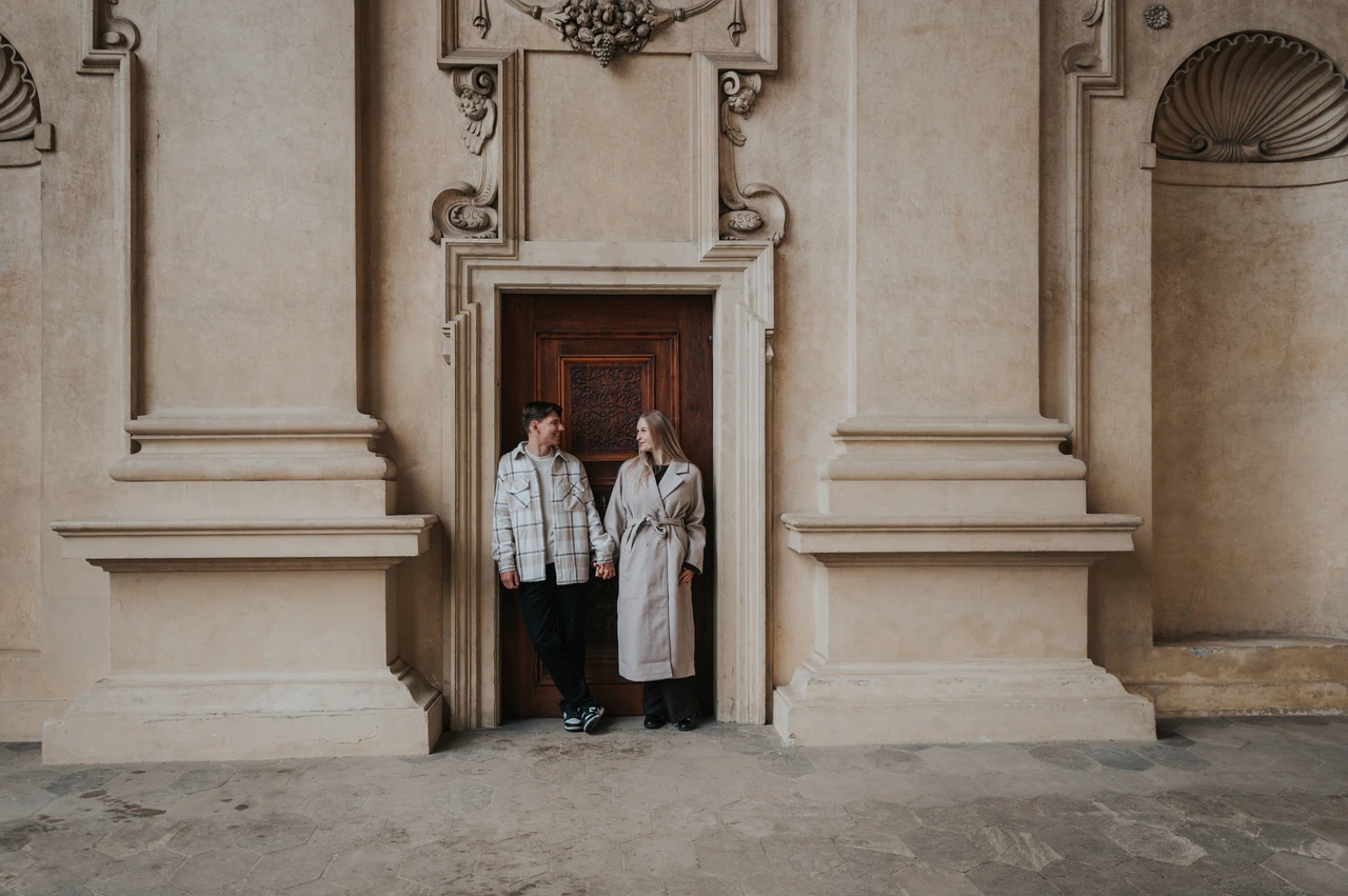 Prague couple photoshoot: framed by the arcade's stonework Wide portrait of the couple framed by the doorway and decorative stone walls during their Prague couple photoshoot.