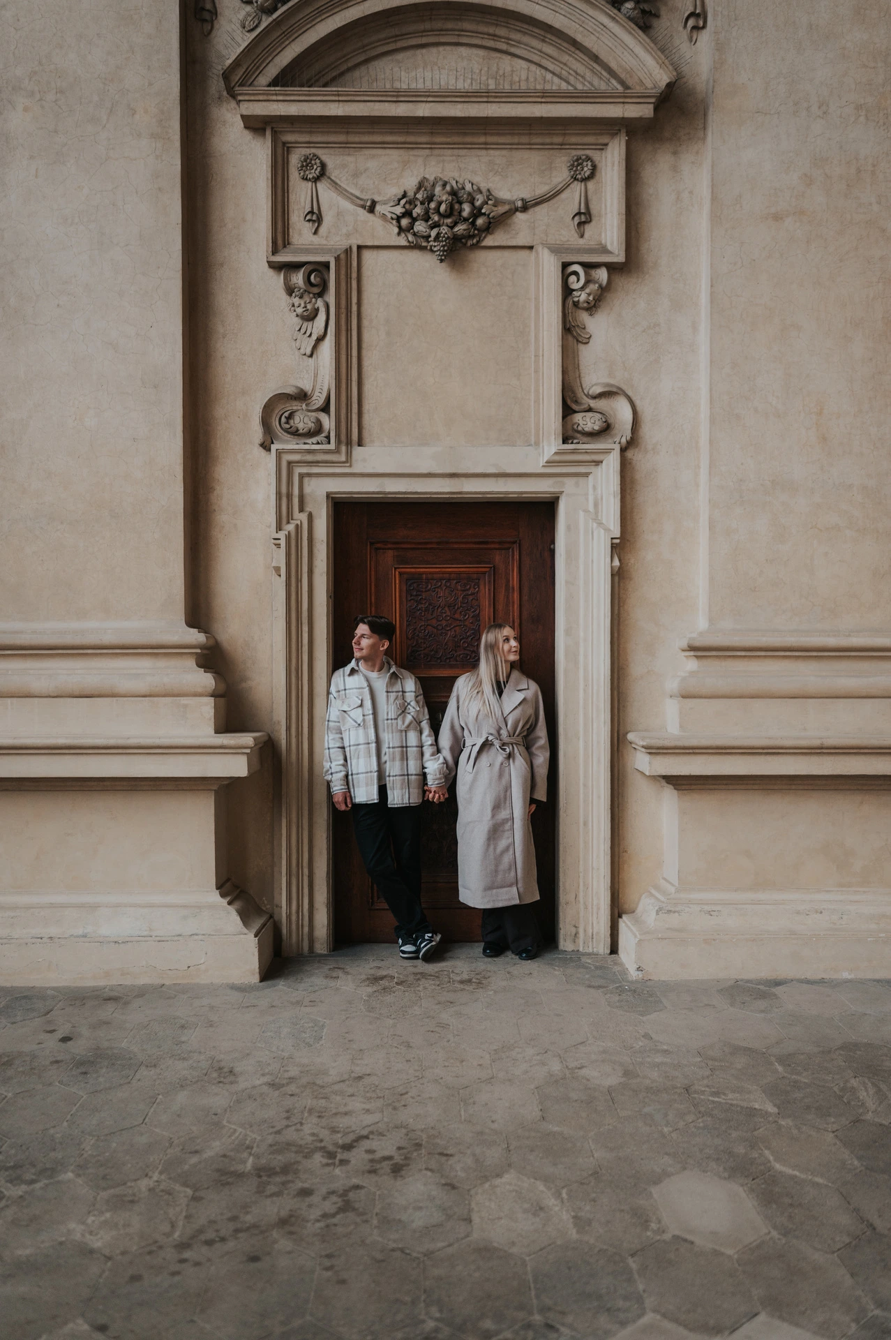 Full-length portrait of the couple together beneath the decorated doorway pediment during their Prague couple photoshoot.