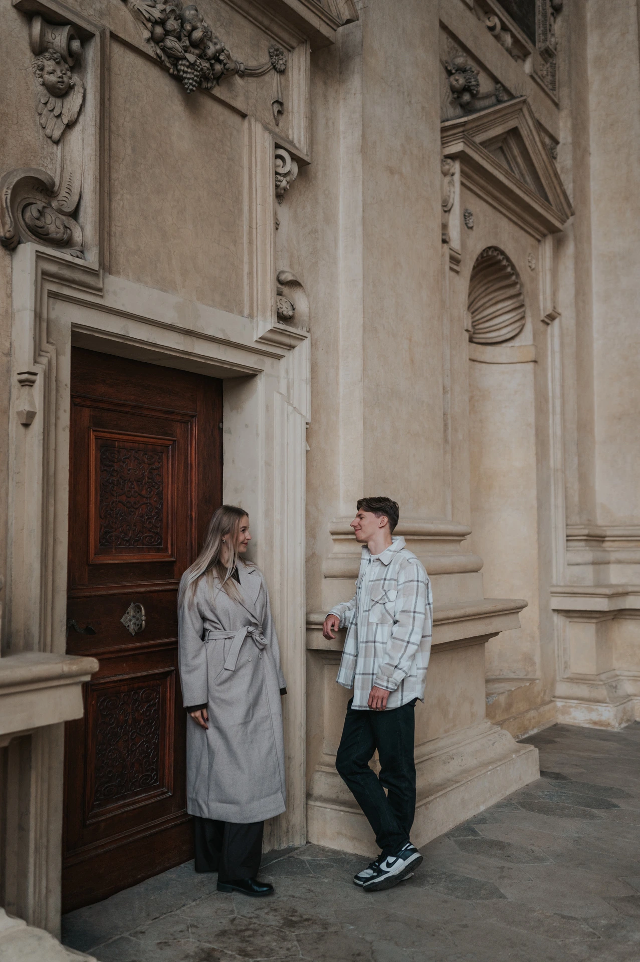 Side view of the couple standing apart beside the wooden arcade doorway during their Prague couple photoshoot.