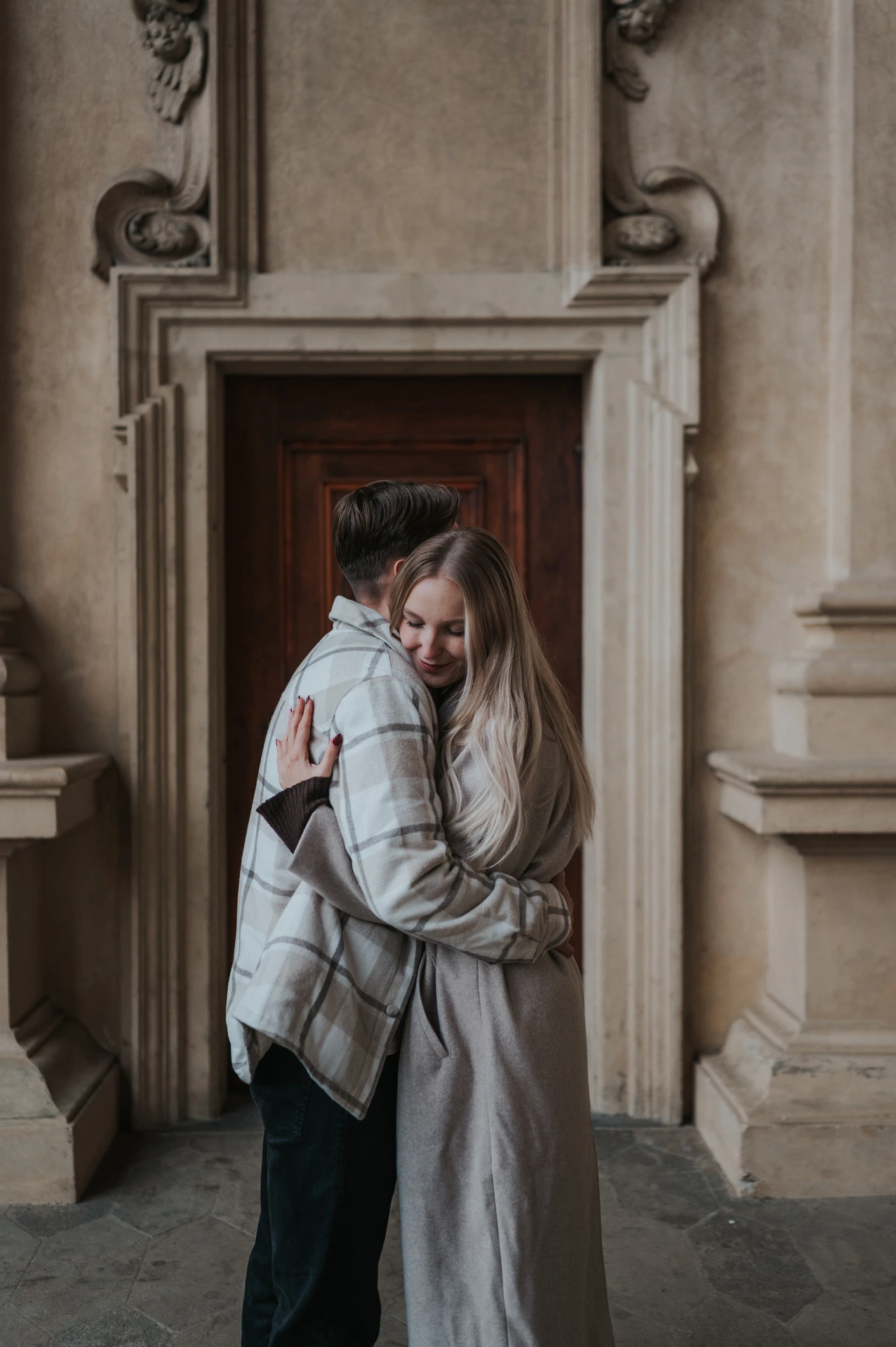 Woman smiling while hugging her partner in the wooden arcade doorway during their Prague couple photoshoot.