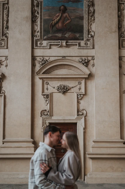 Prague couple photoshoot: an embrace beneath the historic fresco Couple embracing below a painted fresco and an ornate stone pediment during their Prague couple photoshoot.