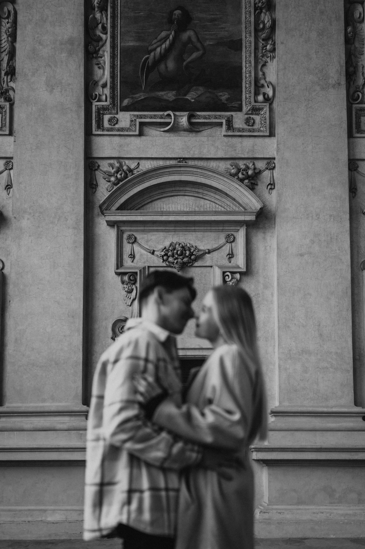 Black-and-white soft-focus portrait of the couple kissing beneath the arcade fresco during their Prague couple photoshoot.