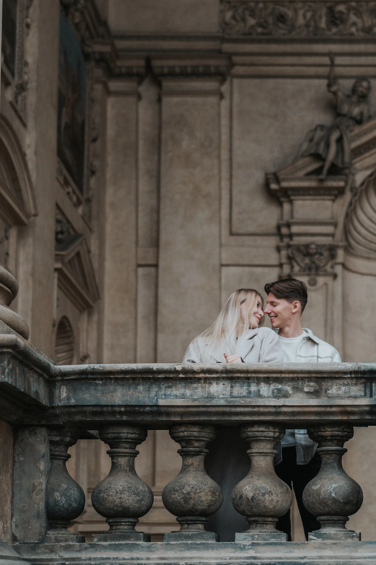 Couple leaning close together behind the arcade's stone balustrade during their Prague couple photoshoot.