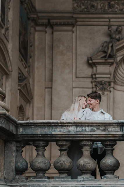 Prague couple photoshoot: a moment behind the stone balustrade Couple leaning close together behind the arcade's stone balustrade during their Prague couple photoshoot.