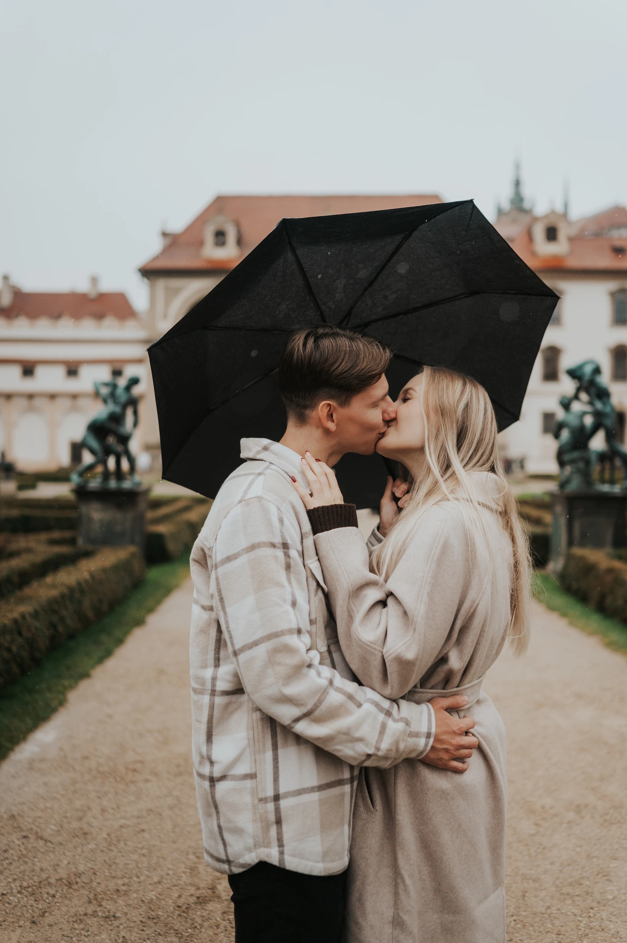 Couple kissing beneath their umbrella with the formal garden behind them during their Prague couple photoshoot.