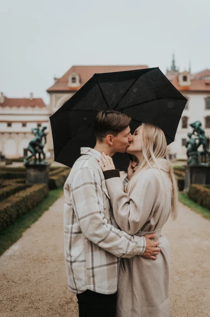 Prague couple photoshoot: a close kiss on the garden path Couple kissing beneath their umbrella with the formal garden behind them during their Prague couple photoshoot.