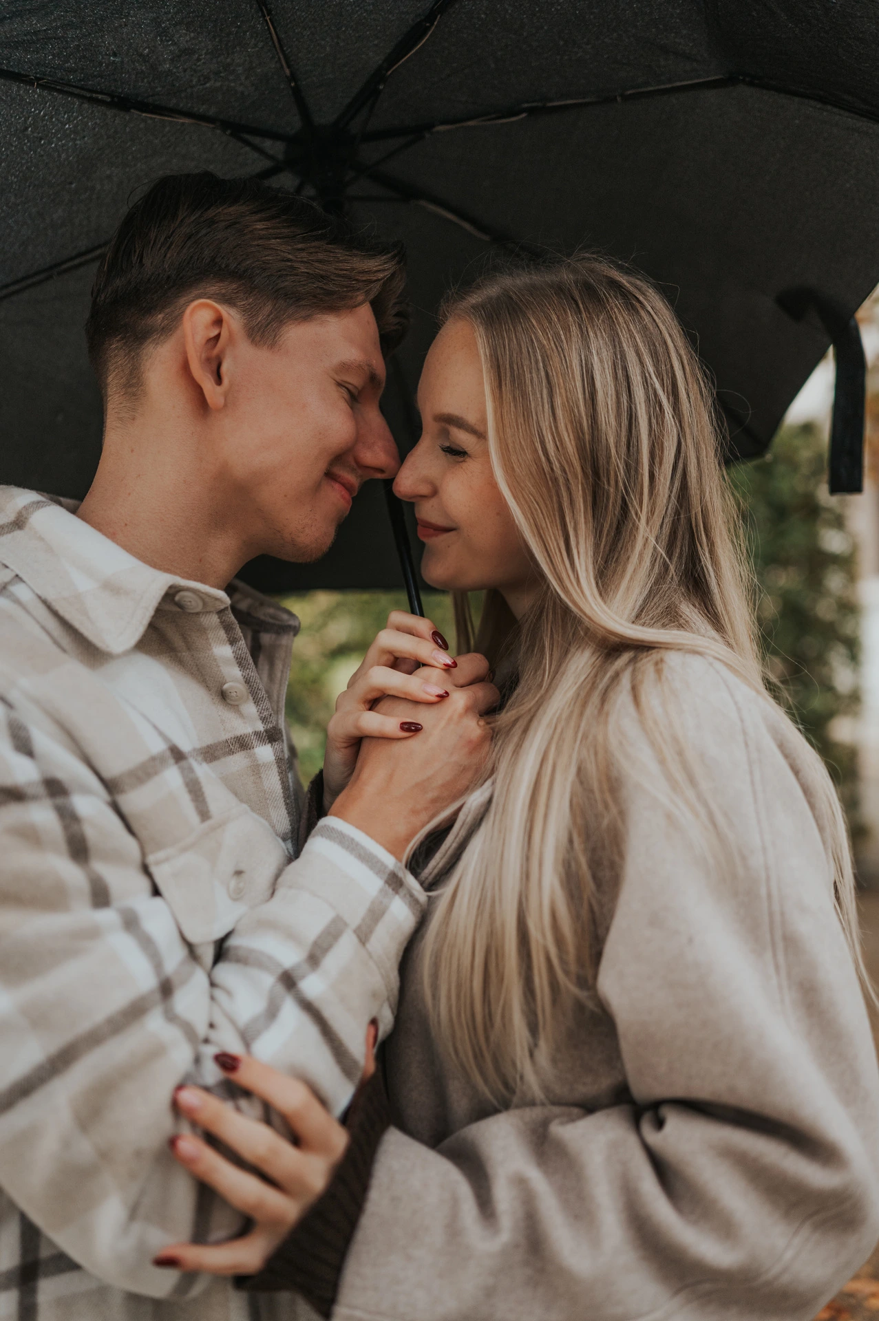 Close portrait of the couple touching foreheads and holding hands beneath their umbrella during their Prague couple photoshoot.