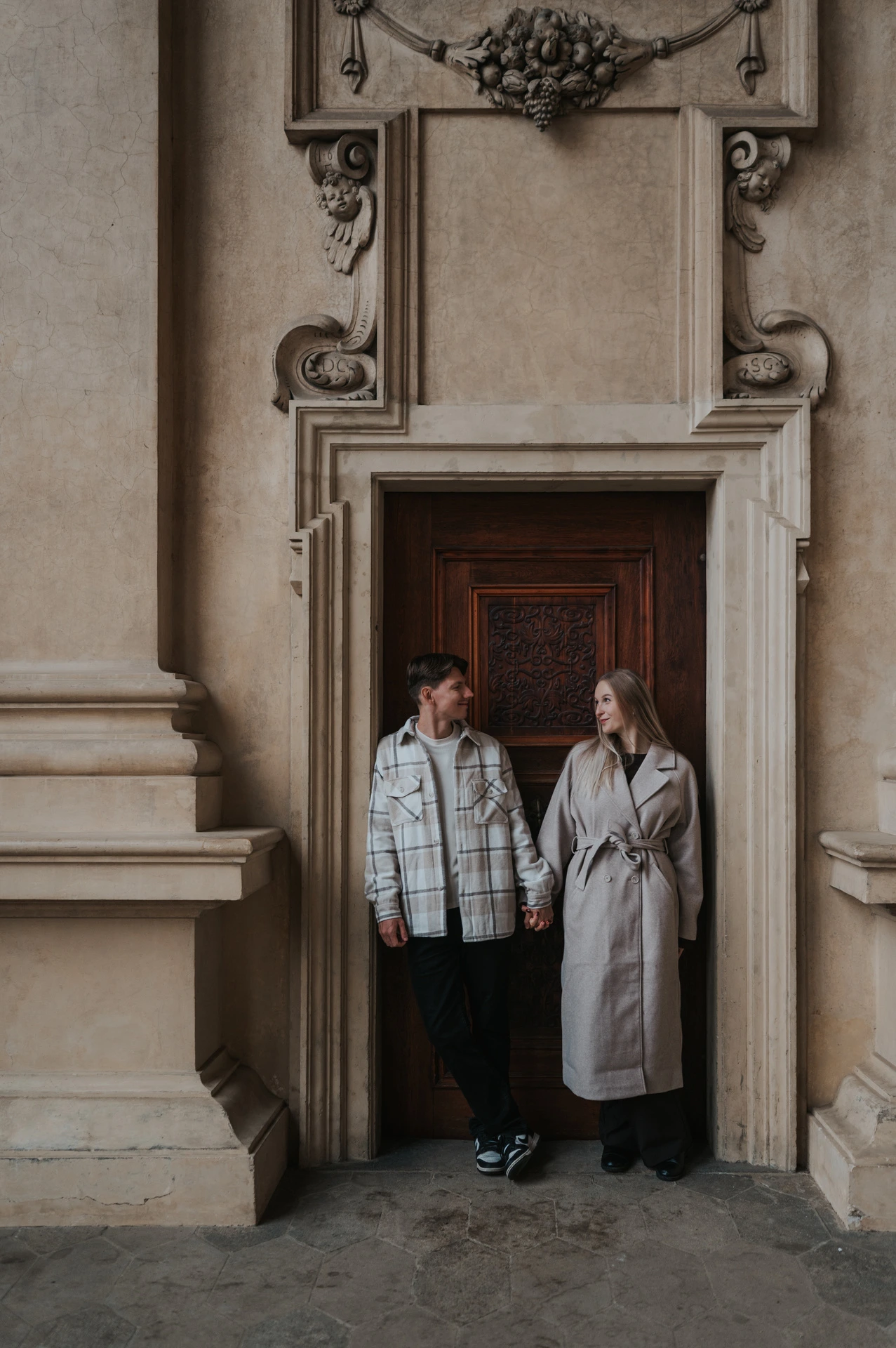 Couple standing side by side in a carved wooden doorway at Wallenstein Garden during their Prague couple photoshoot.