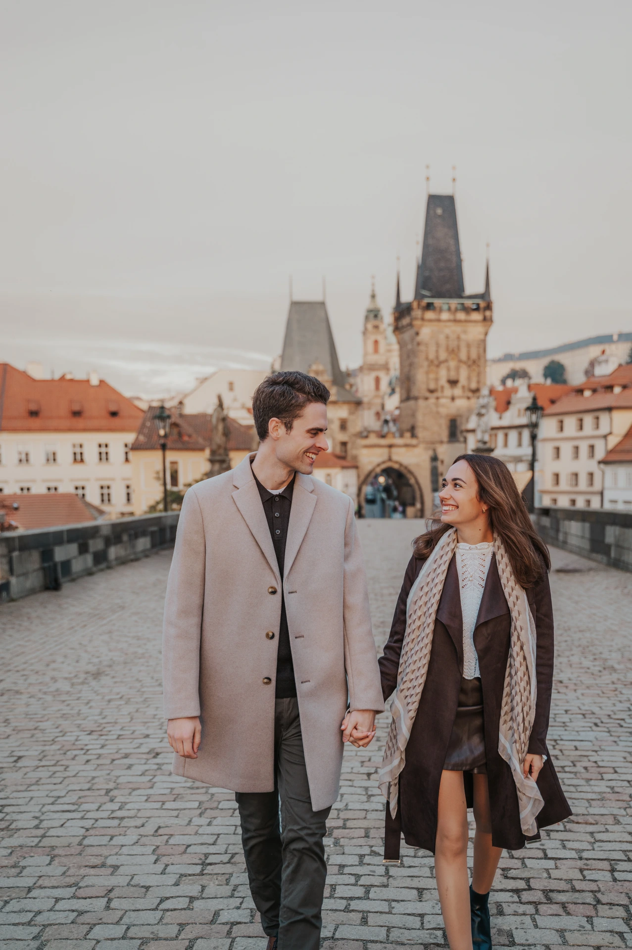Couple smiling at each other on Charles Bridge during an engagement photoshoot in Prague