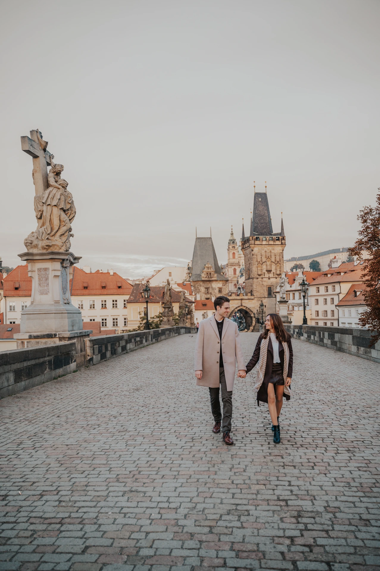 Wide view across the cobbles of Charles Bridge as the couple walk together for their Prague engagement photoshoot