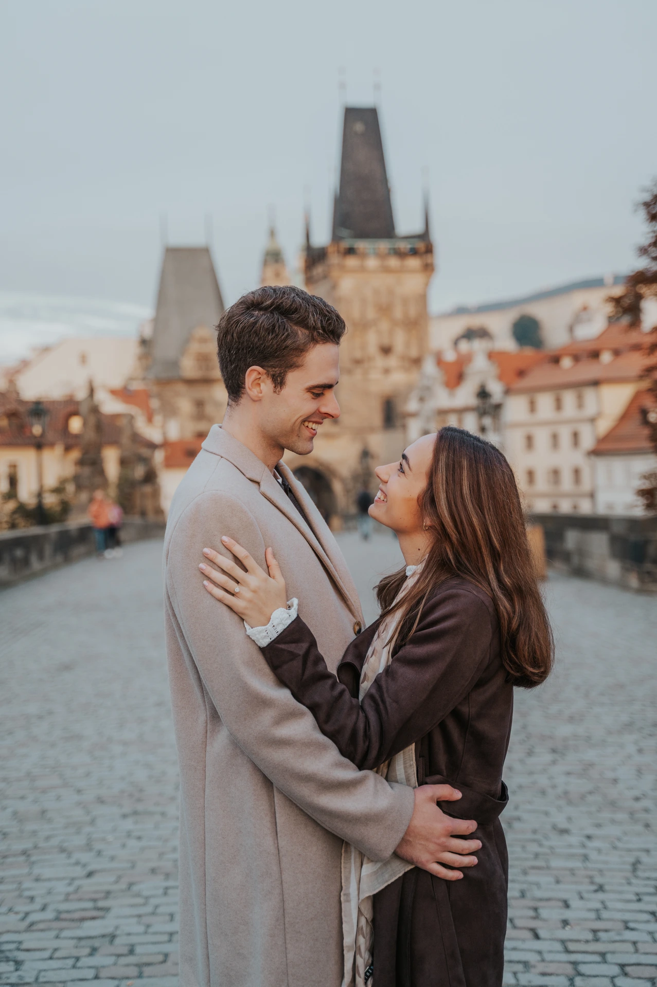 Couple embracing in front of the Charles Bridge towers during their engagement photoshoot in Prague