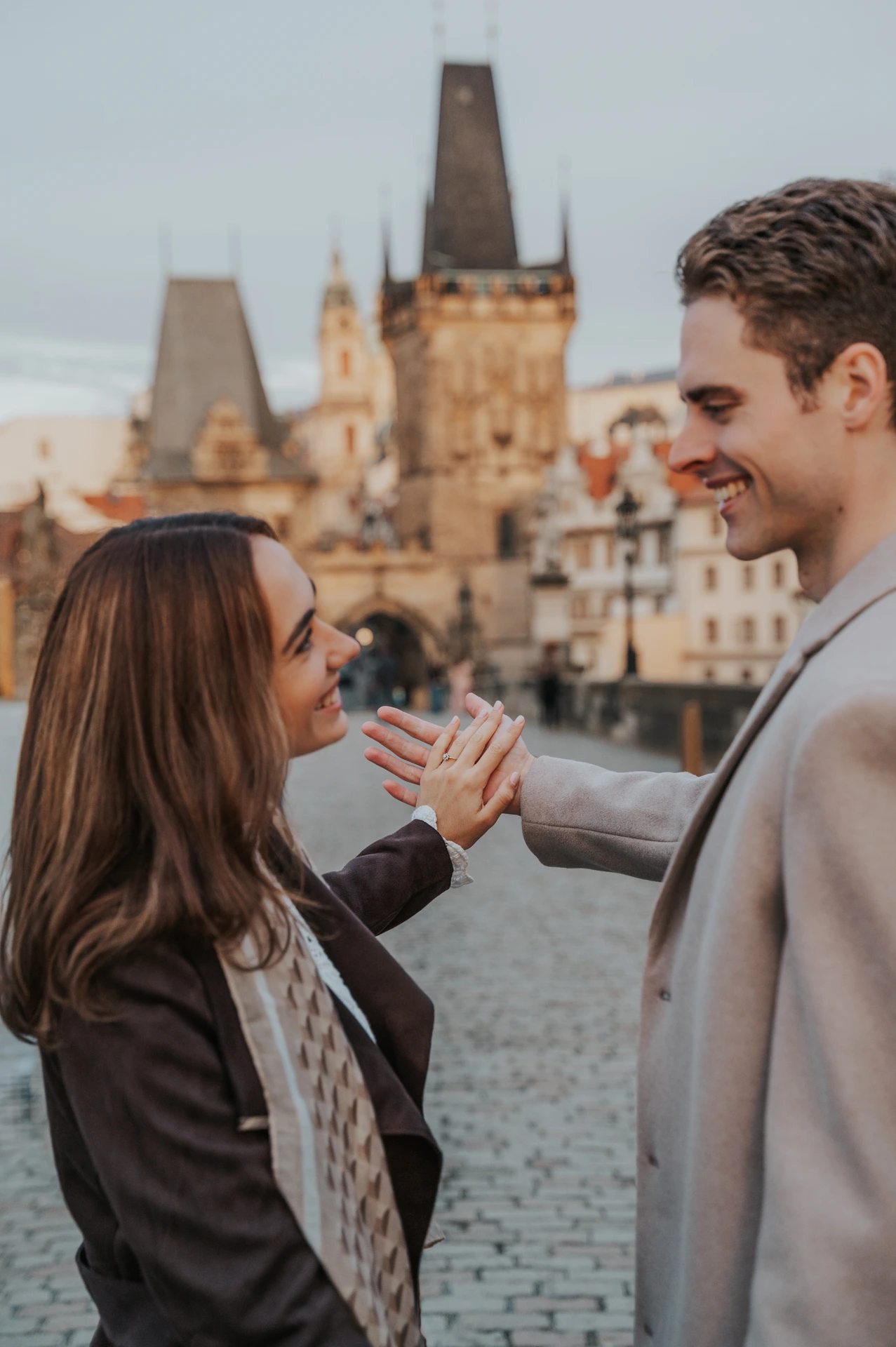 Couple laughing together with a Charles Bridge tower behind them at their Prague engagement photoshoot
