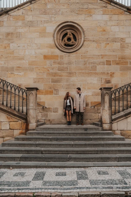 Engagement photoshoot on the bridge stairs Couple standing together on stone stairs beneath Charles Bridge during their engagement photoshoot in Prague