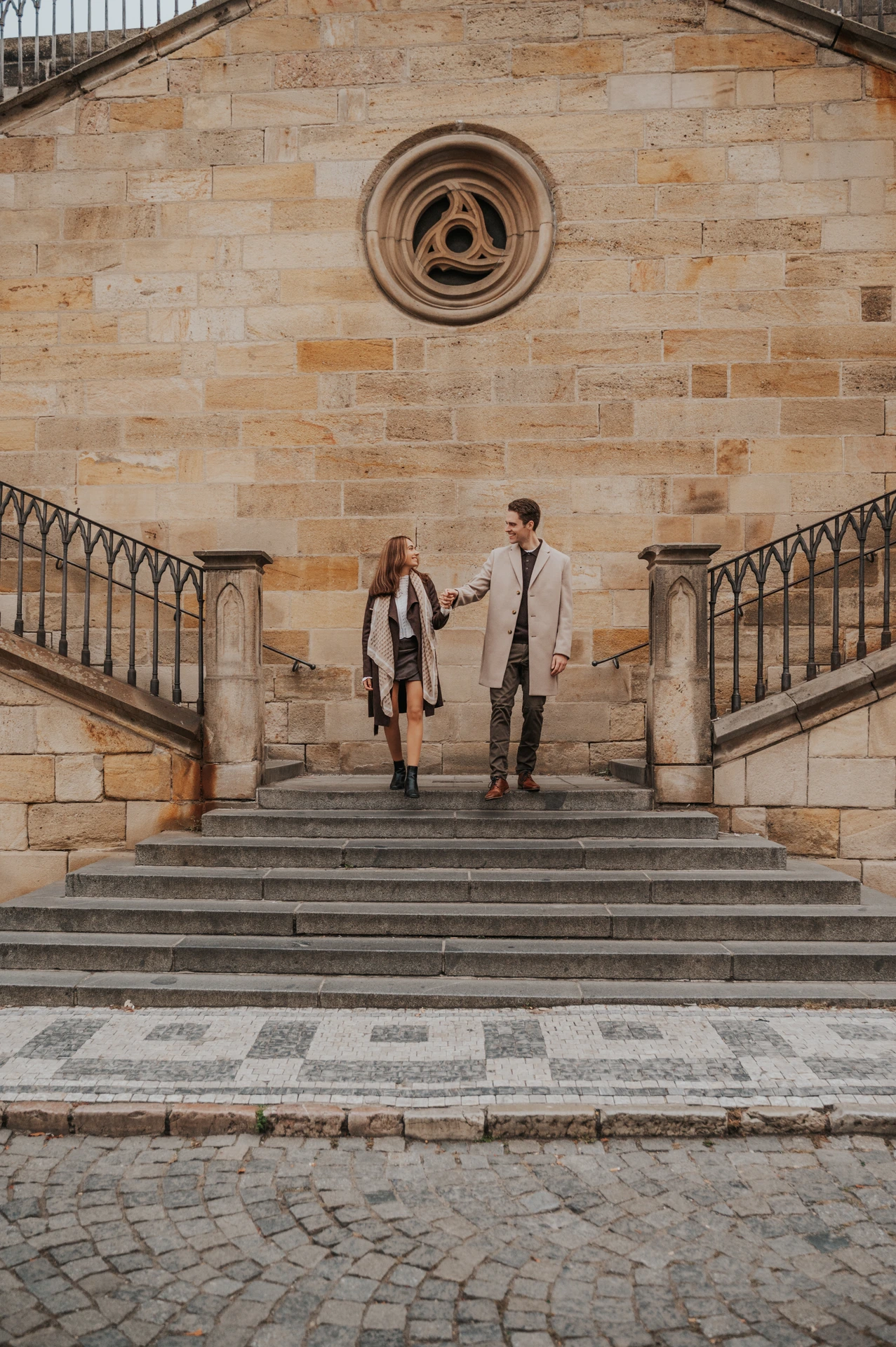 Couple holding hands on the stairs beside Charles Bridge during their engagement photoshoot in Prague