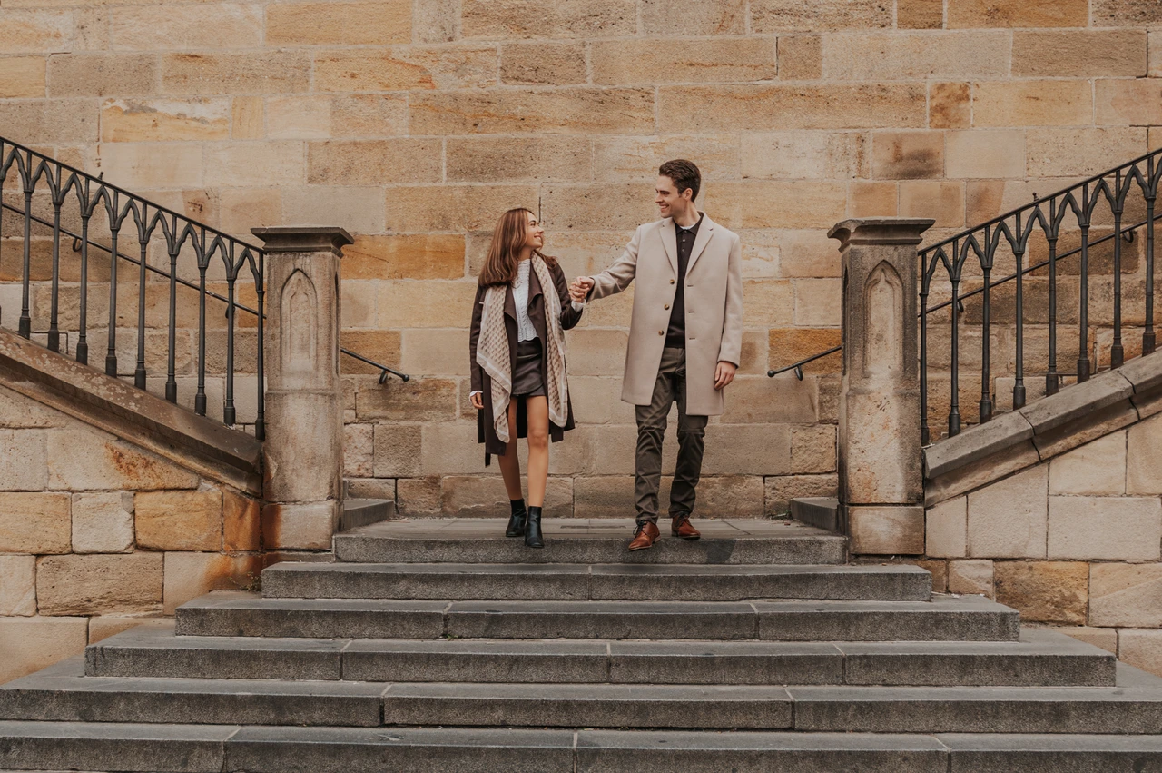 Walking down the Charles Bridge stairs Couple walking down the stone stairs beside Charles Bridge during their Prague engagement photoshoot