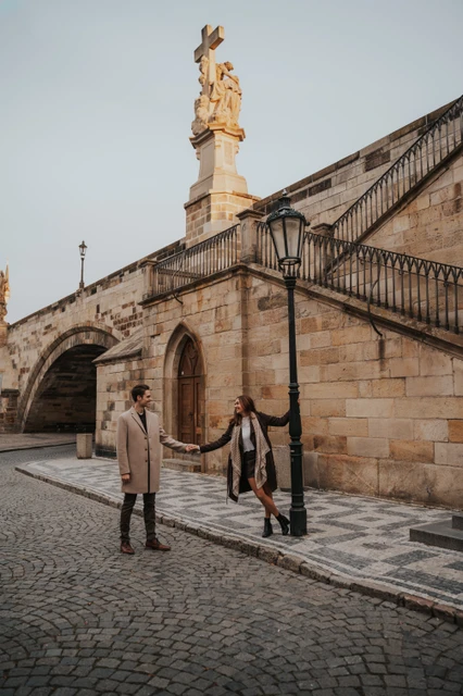 Engagement photoshoot beneath Charles Bridge Couple holding hands beside a stone arch below Charles Bridge at their Prague engagement photoshoot