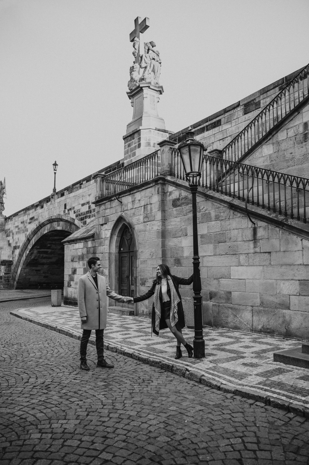 Black and white photograph of the couple beneath Charles Bridge during their engagement photoshoot in Prague