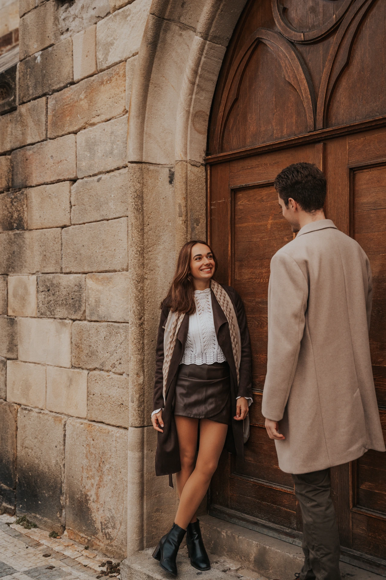 Woman leaning against a wooden door while her partner stands beside her during their Prague engagement photoshoot
