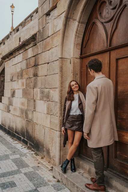 The arched doorway below Charles Bridge Couple beside an arched wooden door below Charles Bridge during an engagement photoshoot in Prague