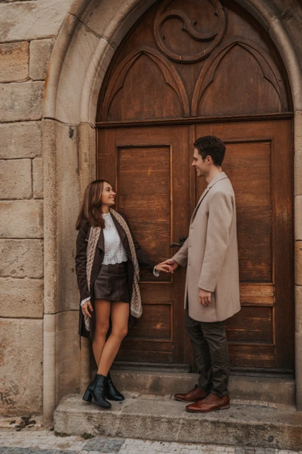 Holding hands by the wooden doorway Couple holding hands in front of a wooden doorway near Charles Bridge at their Prague engagement photoshoot