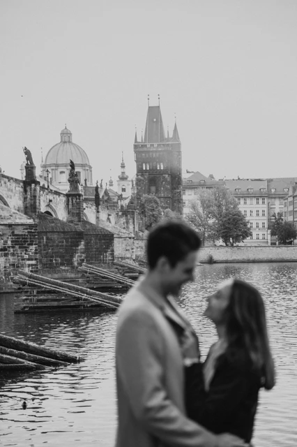 A Vltava portrait in black and white Black and white portrait of the couple beside the Vltava during their Prague engagement photoshoot, with Charles Bridge behind them