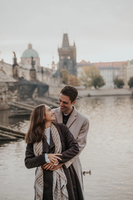 A hug beside the Vltava Couple hugging beside the Vltava with Charles Bridge in the background at their Prague engagement photoshoot