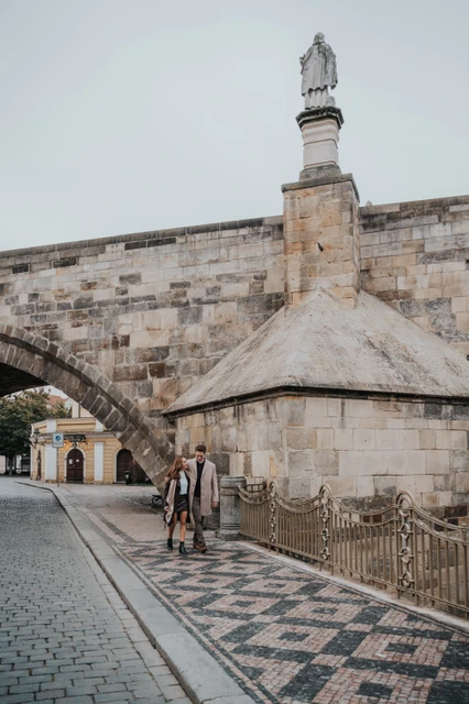Walking beneath the Charles Bridge arch Couple walking below a stone arch of Charles Bridge during their Prague engagement photoshoot