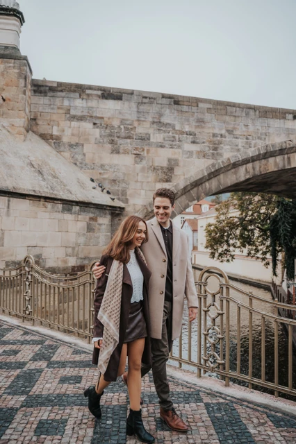 Smiles beneath the Charles Bridge arches Couple smiling side by side below the Charles Bridge arches during their Prague engagement photoshoot