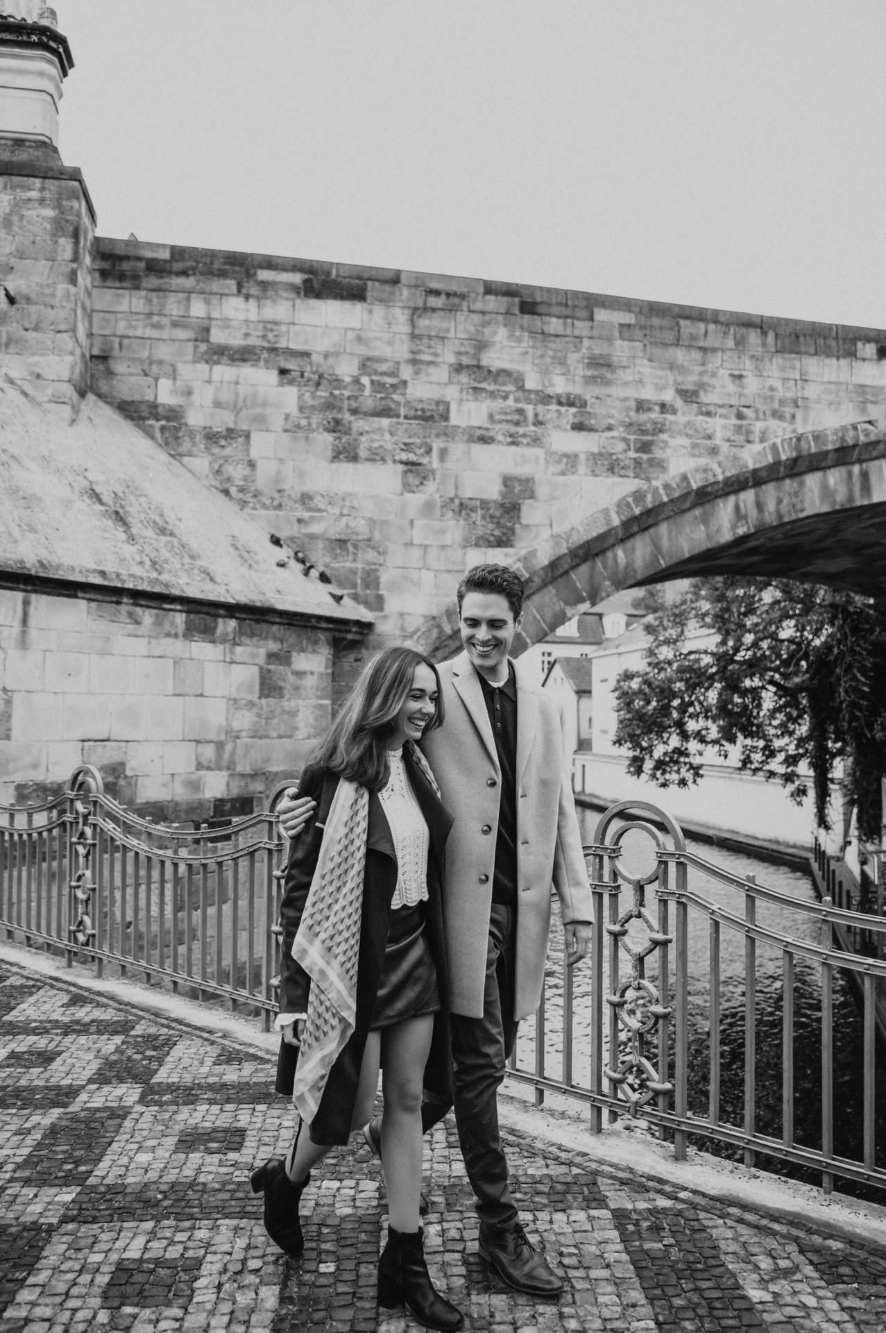 Black and white portrait of the couple below Charles Bridge at their engagement photoshoot in Prague