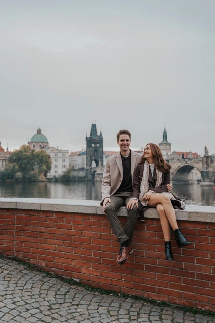 Together on a riverside wall Couple facing the camera from a riverside wall near Charles Bridge during their engagement photoshoot in Prague