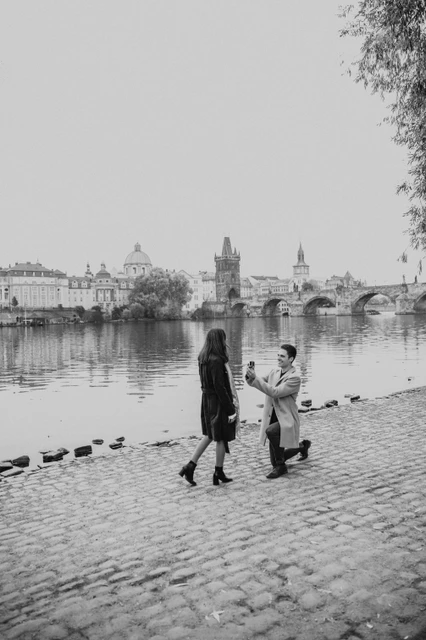 A Prague proposal in black and white Black and white photograph of the man on one knee during the couple's proposal photoshoot on the Kampa riverbank in Prague
